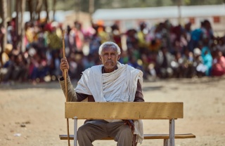 A village elder sits at a desk against the backdrop of a crowd which had gathered.