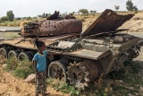 Image of a child stood next to a tank that has been left behind.
